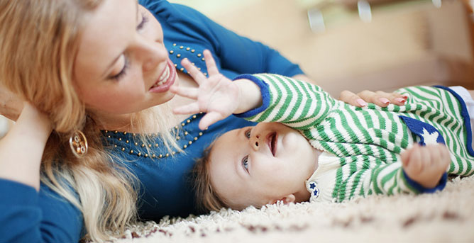 Mother and toddler lying on carpeted floor. Toddler is smiling and reaching up at the mother.